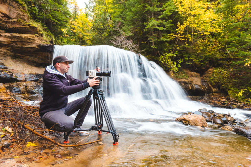 Image of a man using a camera on a tripod in front of a small waterfall